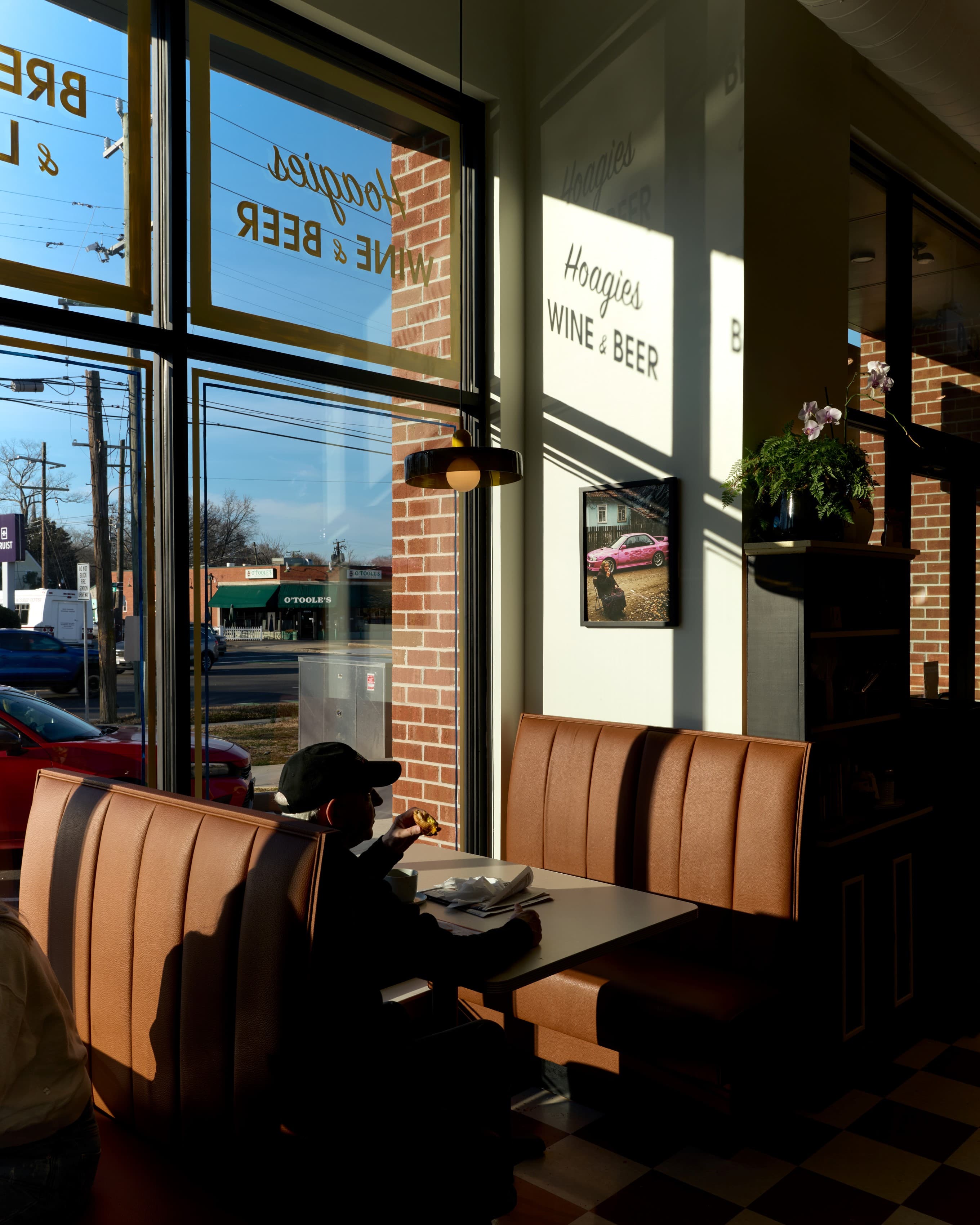 A leather booth beside the storefront window, low winter sun casting the storefront's gold-leaf lettering across the interior wall, the street and a neighboring storefront visible through the glass.