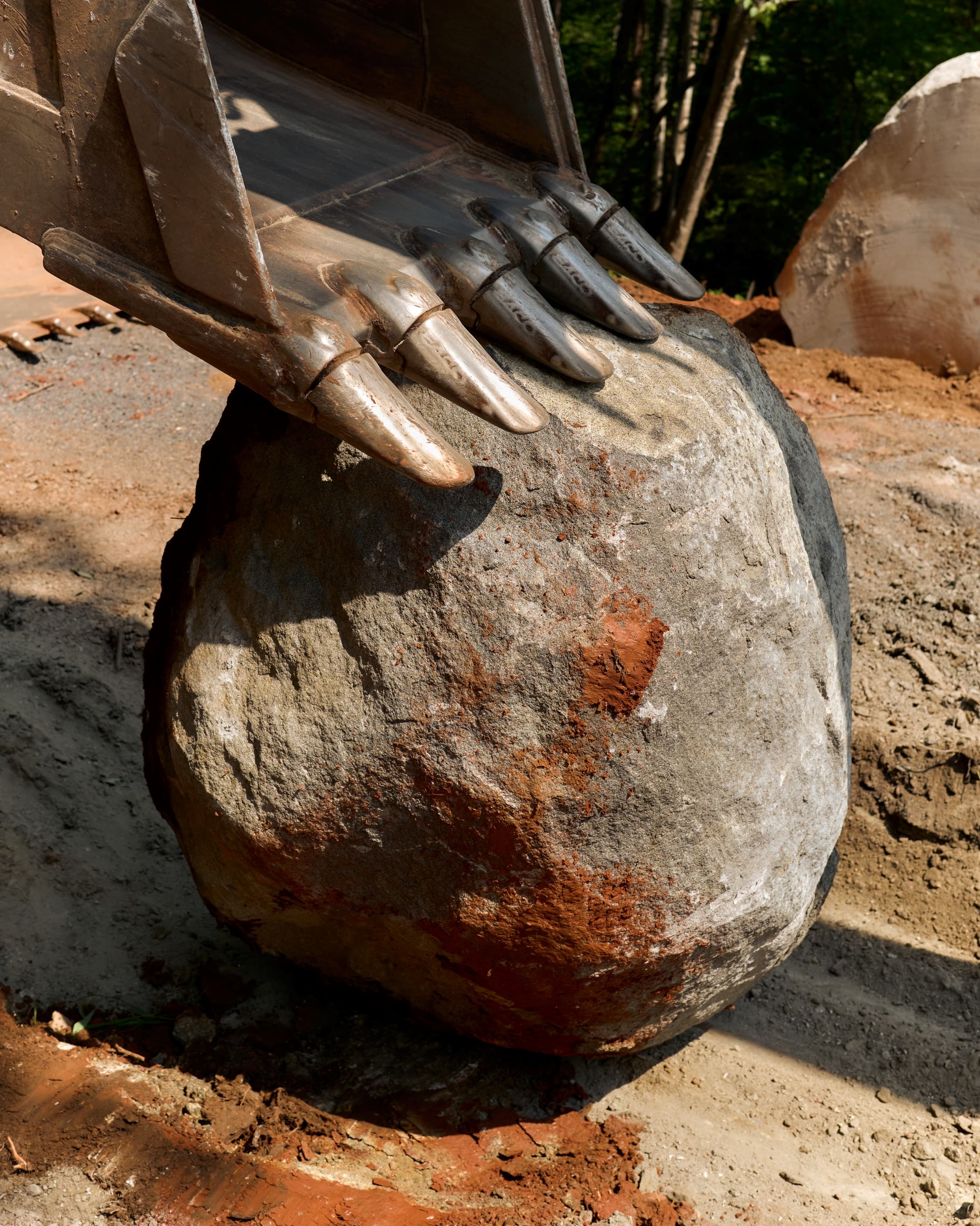 A granite boulder held in an excavator bucket, set aside as foundation pier stone.