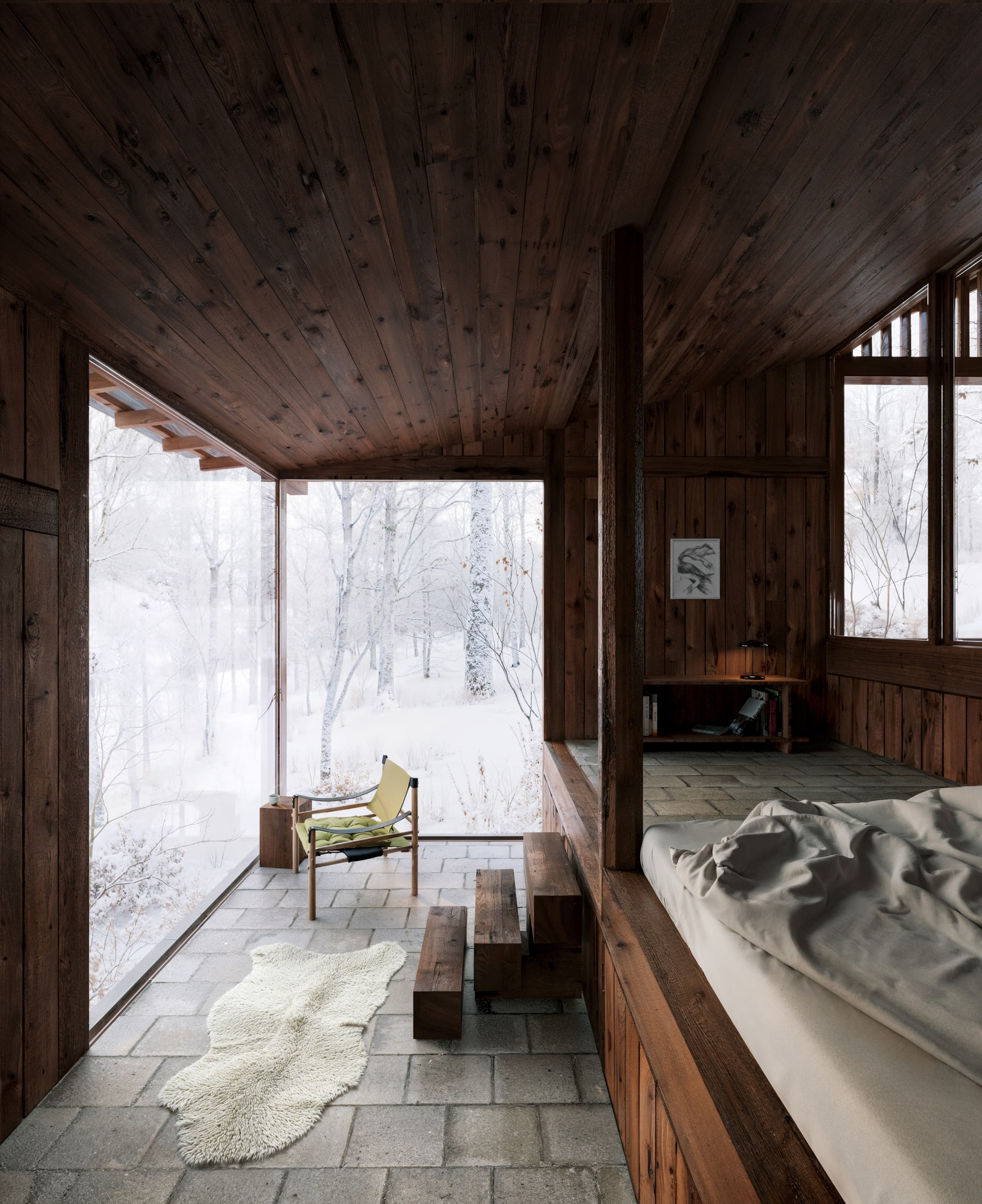A raised sleeping platform beside full-height glazing, snow-covered forest beyond.