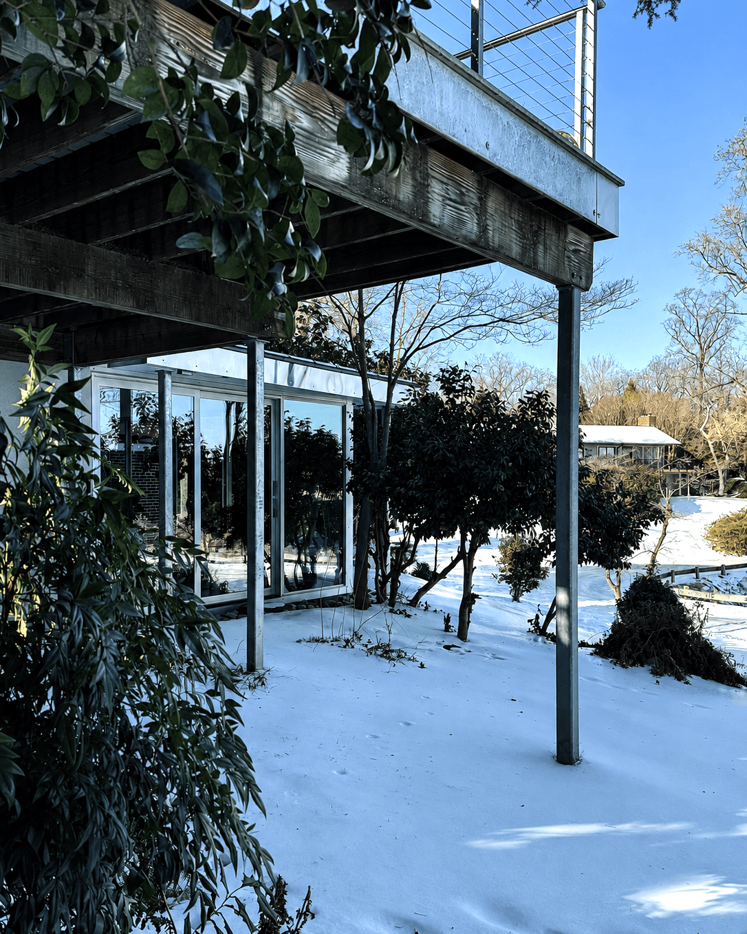 The existing porch above and the new galvanized column and glazing below, seen from the yard in snow.