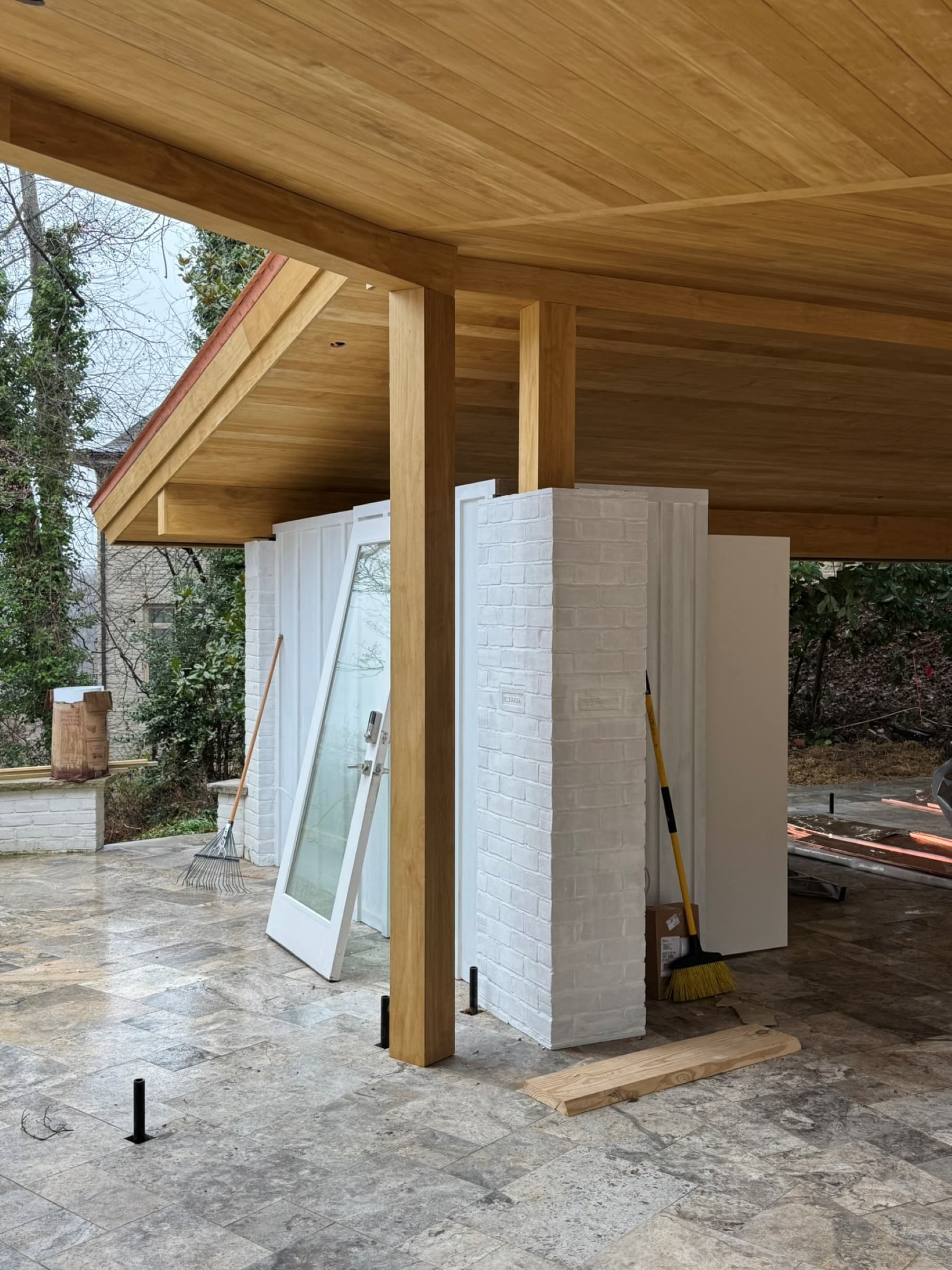 A steel column and Accoya tongue-and-groove soffit of the new roof structure, landing beside a painted-brick pier of the existing house, this corner's construction complete.